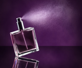 perfume bottle spraying on dark purple background - obrazy, fototapety, plakaty