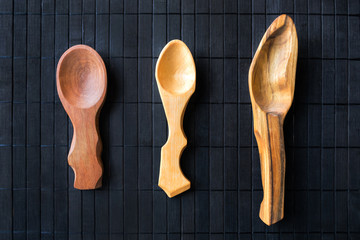 3 three empty handmade wooden spoons from different wood and different sizes on a black wooden background. Beautiful homemade spoons in a rustic style. Wood carving craft