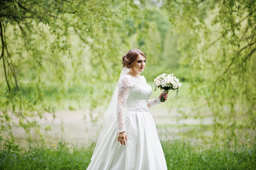 Fototapeta premium Portrait of a beautiful young bride posing with a bouquet outdoor on her own.