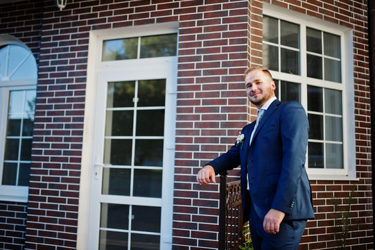 Portrait of a handsome young groom posing with a brick house on the background.