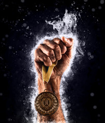 Man's hand in a blue fire is holding up gold medal. Winner in a competition.