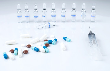 Pharmaceutical medical colorful pills, capsules, ampoules and syringe on white background