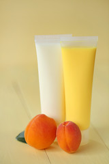 cosmetic with apricot extract.  apricot shower gel and white body cream with apricot extract and apricots fruit on a yellow wooden background. organic natural vegan cosmetics concept