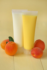 cosmetic with apricot extract. yellow apricot shower gel and white body cream with apricot extract and apricots fruit on a yellow wooden background. organic natural vegan cosmetics concept