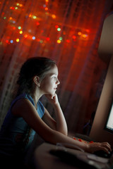 Adorable little girl looking at the computer monitor, on a background of blurred Christmas lights