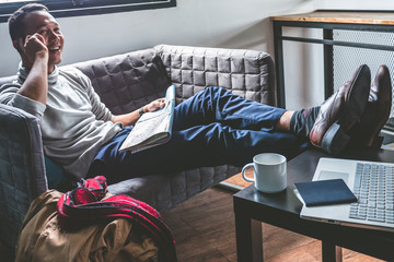 Obraz premium Asian young man using smart phone and map on sofa. Traveler man planning vacation. Travel concept.