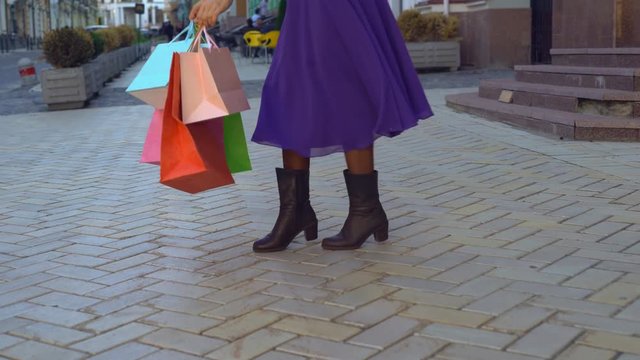 close-up of feet. a happy girl in autumn winter boots sants with happiness. the girl has a bright, long, fiolet dress. a lot of bright paper bags can be seen in the frame. the woman is dancing on the