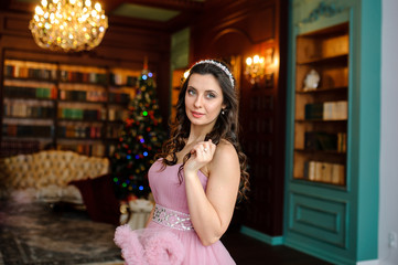 Pretty girl in pink dress near the Christmas tree.
