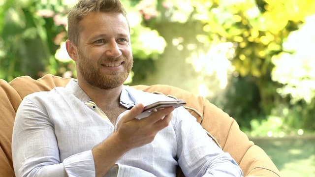 Handsome man relaxing on bean bag chair and chatting on loudspeaker
