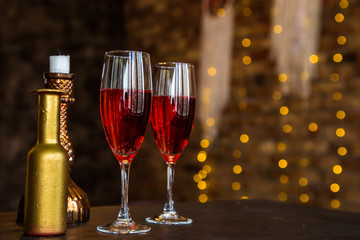 Two glass glasses, a decanter with pink champagne, wine, stand on a blurry background of a brick wall, candles, a herring in the background, bokeh. Romantic evening, date. Place for the inscription.