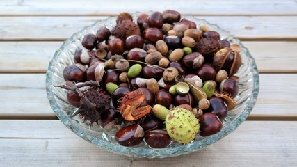 autumn background with chestnuts and acorns in a glass bowl
