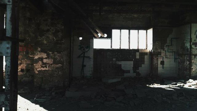Interior motion real time shot of a long abandoned and partly demolished industrial factory in Greece.Sun light creeping through holes in the wall.