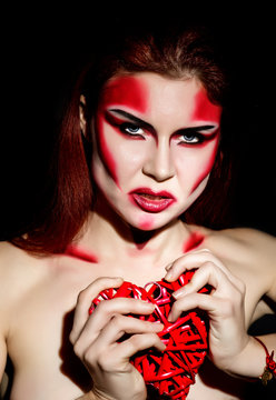 Beautiful sexy devil girl with professional make-up. Fashion Art design. Attractive woman bites the heart