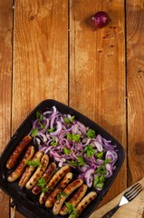 Obraz na płótnie Canvas Fried sausages with onion and parsley in a pan on wooden background