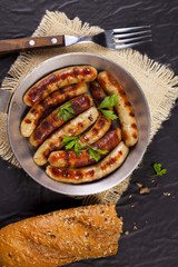 Fried sausages with parsley, bread and fork in a pan on black background