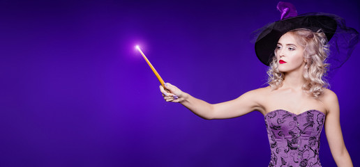 A beautiful woman, blond in a good witch costume on a purple background, holds a magic wand and conjures, focus. Young girl. Halloween