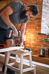 Carpenter drilling a hole in a board in a room with loft interior.