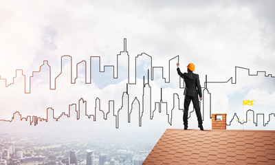 Man architect draw silhouette of modern city on blue sky. Mixed media