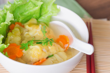 Close up minced pork and shrimp wonton soup or dumpling in white bowl on wood table. Homemade delicious dumpling soup for breakfast or lunch or dinner. Wonton or dumpling soup is popular Chinese food.