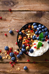 Obraz na płótnie Canvas Tasty homemade granola, yogurt, fresh organic berries, pomegranate, mint on rustic wooden background with copy space, top view.