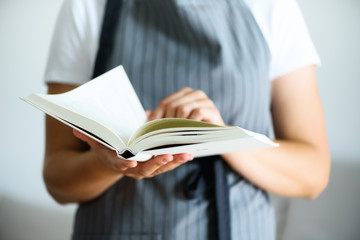 Girl wearing grey apron and reading book. Lifestyle concept