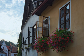Fototapeta na wymiar Windows decorated with red flowers in flower boxes during summer sunset. Old town of Cesky Krumlov, Czech Republic