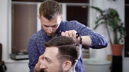 Man standing in salon and cutting hair to client sitting in chair