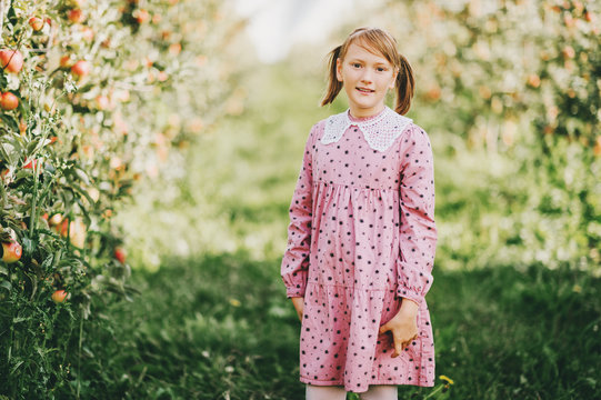 Kid girl playing in apple orchard, wearing pink vintage dress