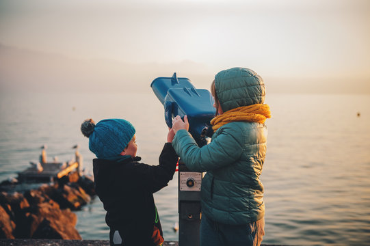 Little kids looking at coin operated binocular by Geneva lake in wintertime