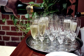 Close-up of a strong waiter's hand pouring alcohol champagne into a glasses on a tray. Champagne bottle. Drinks and luxury concept