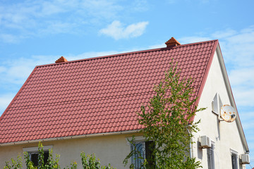 Close up on red metal roof with white, plastic rain gutter system, chimney and rustic antenna. Metal Roofing Construction.