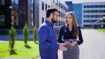 Two entrepreneurs smiling and talking. Male and female cheerful business people communicating and smiling at office building in the street.