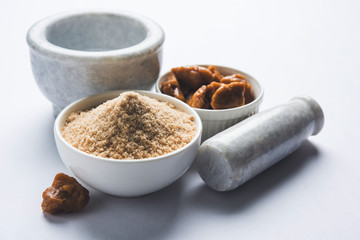 Asafoetida cake and powder or Hing or Heeng which is an important ingredient in Indian food recipes with big wooden spoon and mortar, selective focus