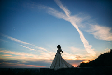 Young girl in wedding dress on city background at sunset. Summer