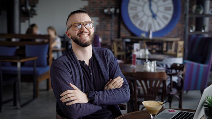 An adult man in glasses, like a hipster, who drinks a non-alcoholic cocktail watching video clips on a laptop in a social network and loudly laughing