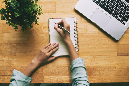 High angle view of unrecognizable businesswoman taking necessary notes in notepad while preparing for important meeting at modern office