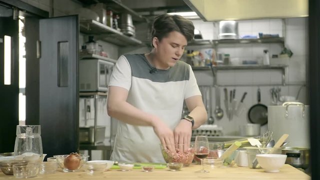 Emotional chef in a cafe in a white T-shirt mince forcemeat in transparent deep bowl on a cutting board