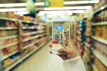 Woman doing grocery shopping at supermarket and viewing offers with help of augmented reality app,...