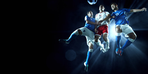 Soccer players performs an action play on a dark background. Soccer players fight for the ball. Players wears unbranded sport uniform.