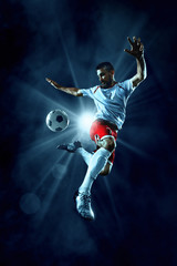 Fototapeta na wymiar Soccer player performs an action play on a dark background. Player wears unbranded sport uniform.