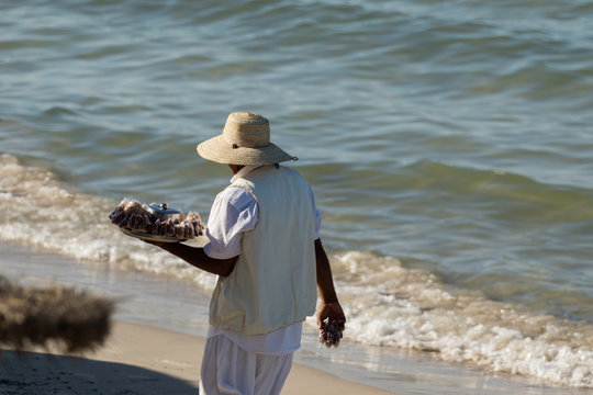 An indigenous man with a hat sells nuts on the beach