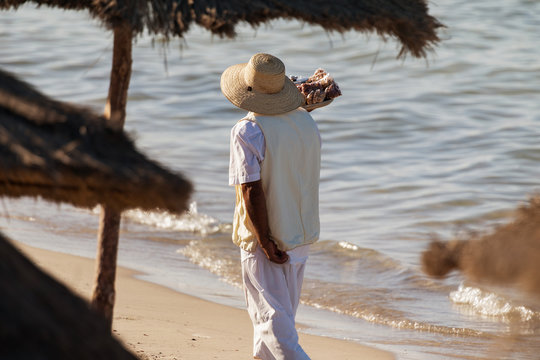 An indigenous man with a hat sells nuts on the beach