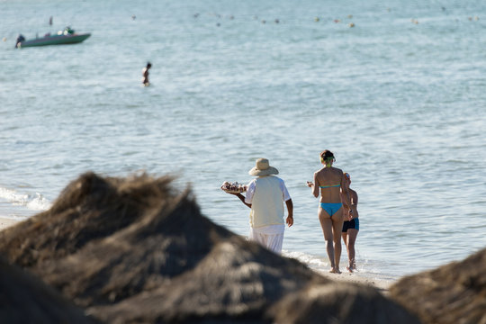 An indigenous man with a hat sells nuts on the beach