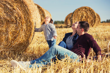 Happy young family with 2 year old girl next to hay bales in harvested field
