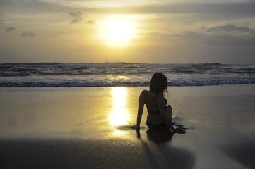 Fototapeta na wymiar silhouette of young woman lying on sand looking to sea sunset horizon with beautiful sun