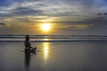 Naklejka na ściany i meble free woman sitting looking to sea sunset practicing yoga and meditation at beautiful Asian beach