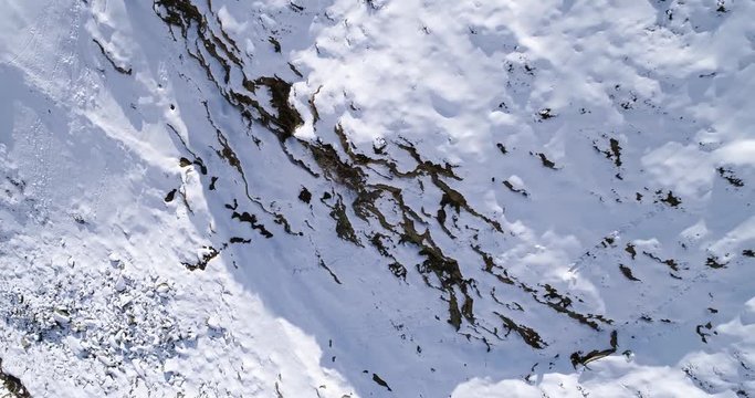 aerial overhead flying moving forward over snowy mountain ridge valley establisher. Outdoor snow alpine wild nature scape in winter top view with sun and shadows. 4k drone flight establishing shot