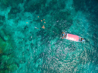 Aerial view of turquoise clear water, speedboat above coral reef, swimming and snorkeling people....