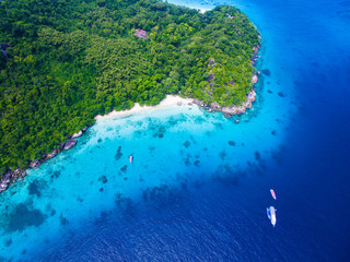 Top aerial view of isolated beautiful tropical island with white sand beach, blue clear water and granite stones. Also top view of speedboats above coral reef. Similan Islands, Thailand.