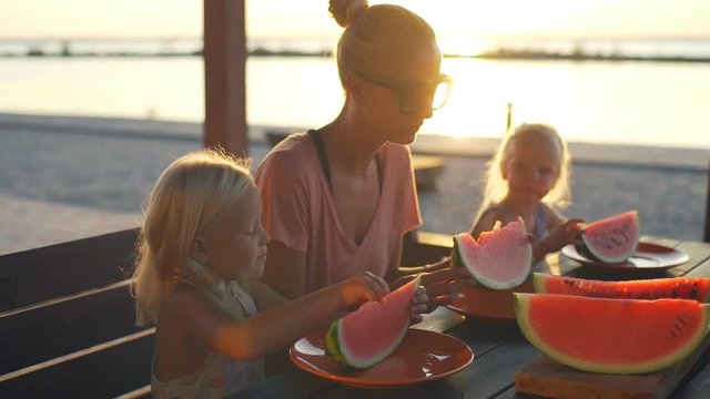 Mother with blonde babies eat watermelon enjoy sunny day rapid slow motion 